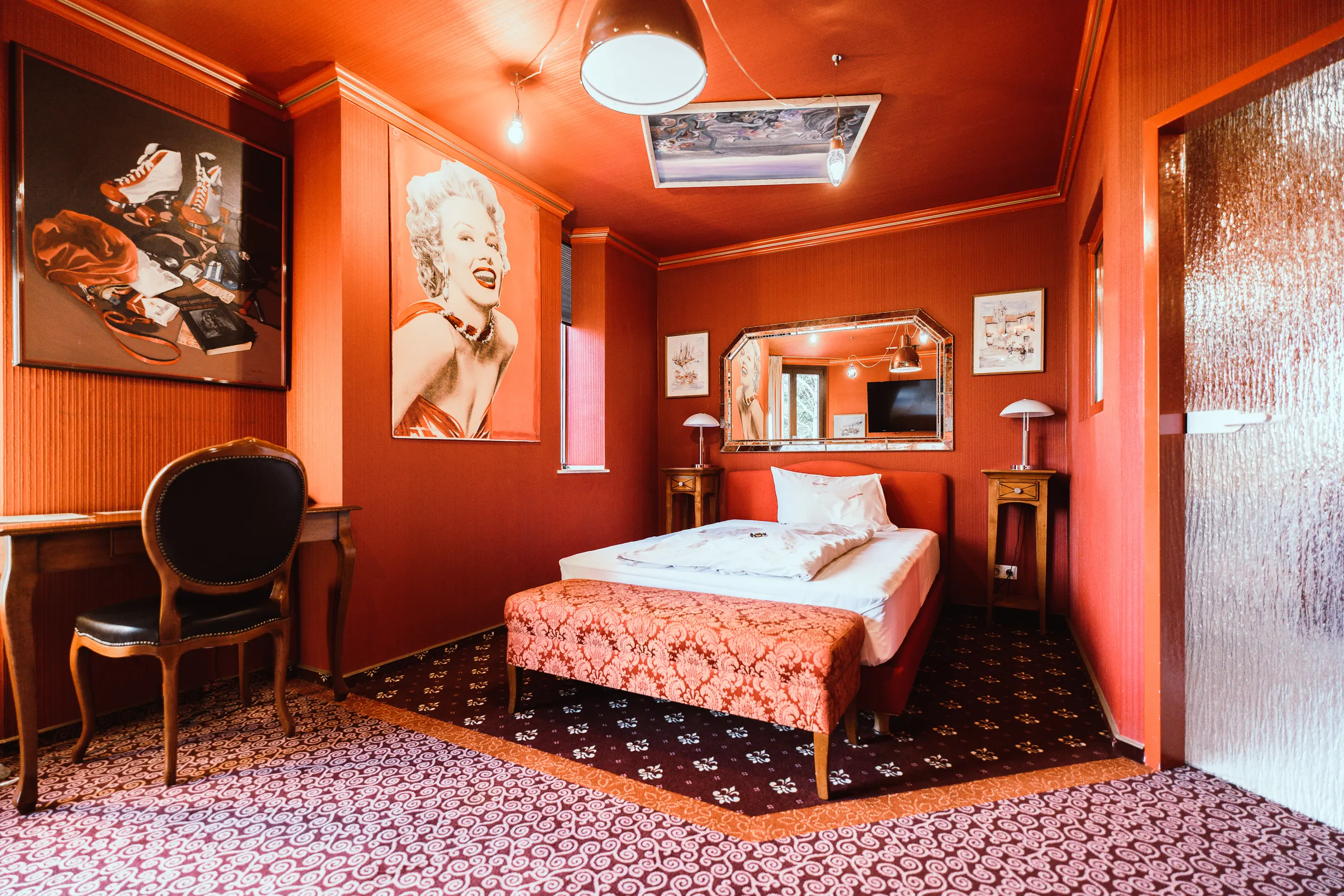 Our “Tabu” spa room is an extravagantly designed space, entirely decorated in rich shades of red, featuring a bed in the center, patterned rugs, and eye-catching vintage-style artwork on the walls.