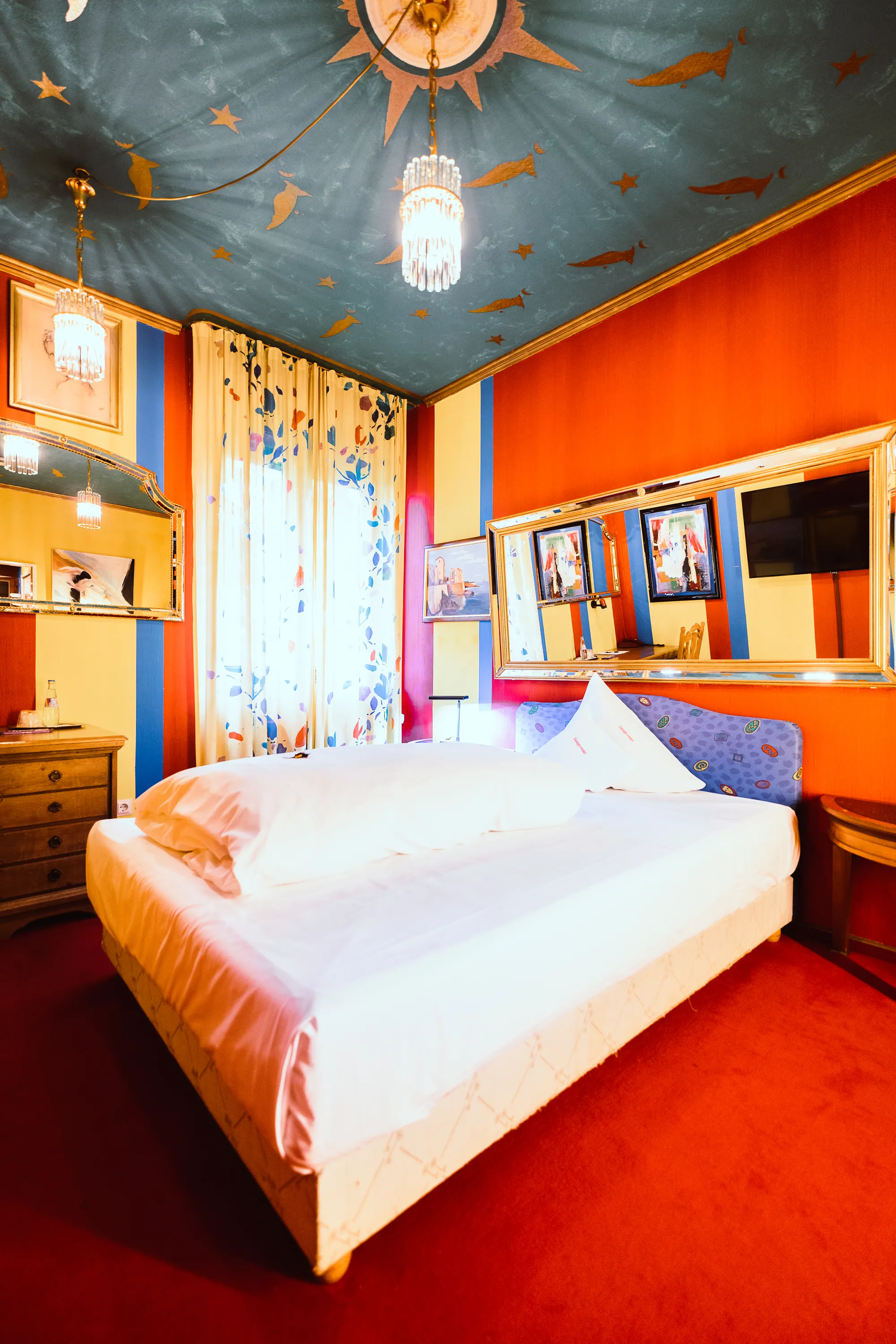 Bed in the “Trance” themed room with a purple patterned headboard and gold-plated wall mirrors.