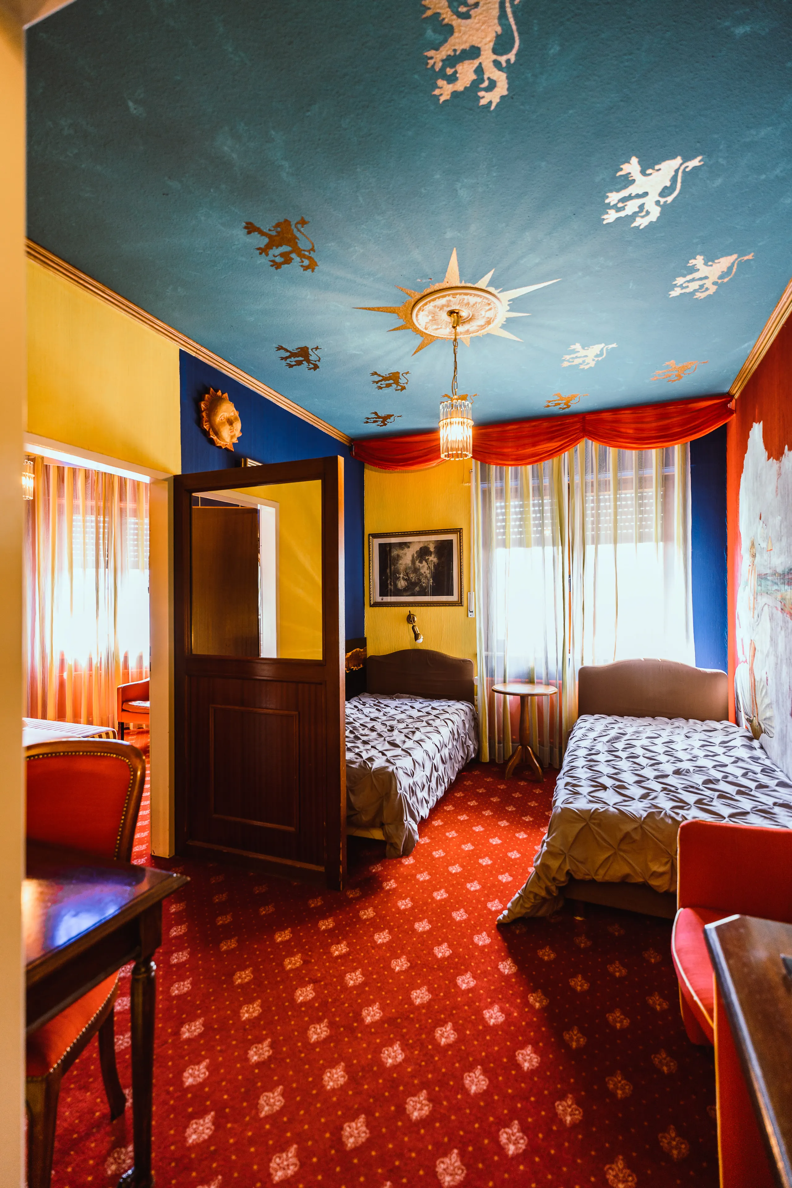 “Unikat” Family Room with two single beds under a blue-and-gold lion-patterned blanket and colorful walls.